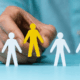 A hand selecting a specific yellow figure among white silhouettes, representing the importance of ICP definition before starting Email, LinkedIn, or ABM campaigns.