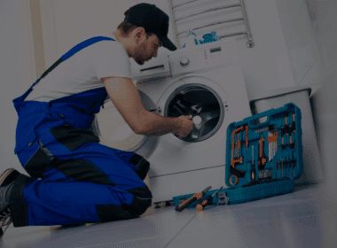A professional technician repairing a washing machine with a toolkit, illustrating how appliance repair services can save you money by extending equipment lifespan.
