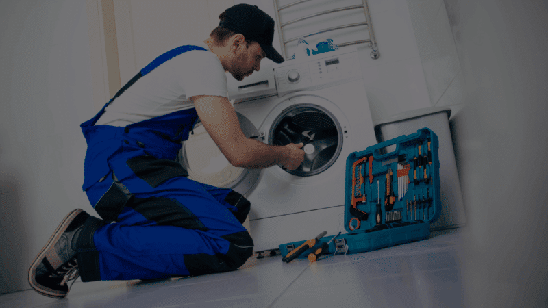 A professional technician repairing a washing machine with a toolkit, illustrating how appliance repair services can save you money by extending equipment lifespan.