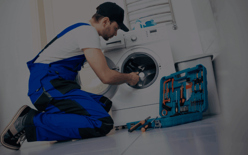 A professional technician repairing a washing machine with a toolkit, illustrating how appliance repair services can save you money by extending equipment lifespan.